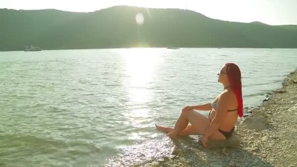 Una joven está descansando en la orilla de un lago de montaña al atardecer. — Vídeo de stock