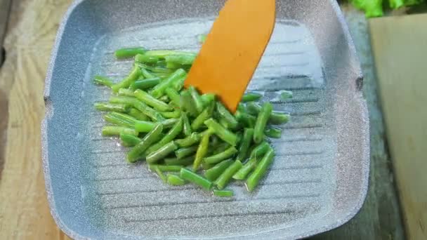 Una mano femenina revuelve un frijol verde frito en aceite con una espátula de madera — Vídeo de stock