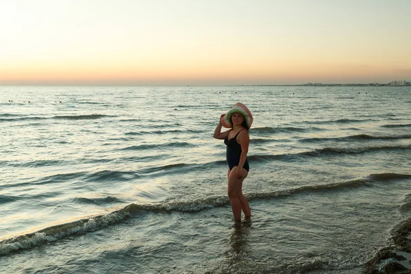 Een vrouw in een hoed loopt langs de kust bij zonsondergang. — Stockfoto