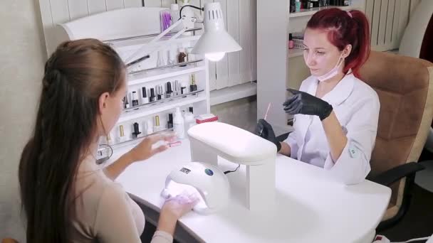 Manicure vrouw in cosmetische bad is het aanbrengen van gel op klanten nagels. Het meisje droogt haar nagels in een ultraviolette lamp. — Stockvideo