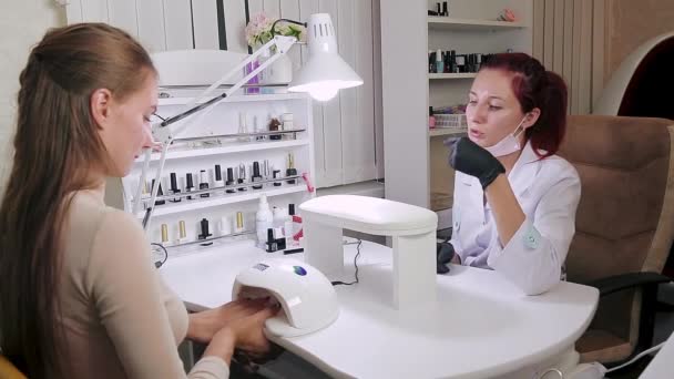 Cliente menina de um salão de beleza seca as unhas em uma lâmpada ultravioleta — Vídeo de Stock