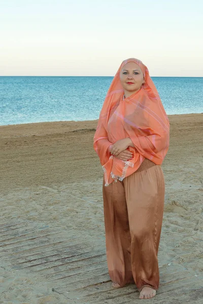 Una joven musulmana en un chal rosa camina por la costa del mar — Foto de Stock