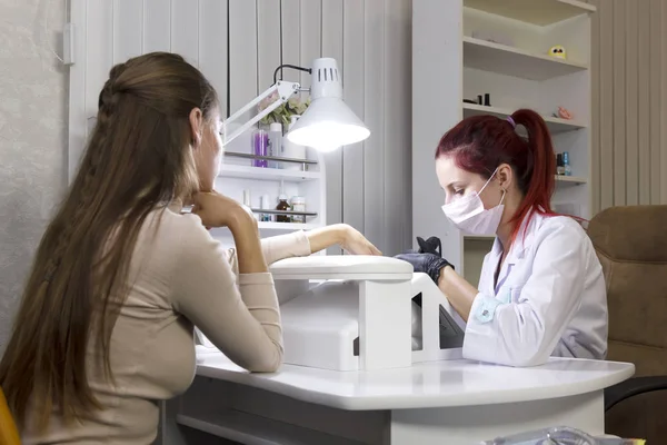 Ein Maniküre-Arzt verarbeitet eine Nagelhaut auf den Nägeln eines Klienten, bevor er das Gel aufträgt. — Stockfoto