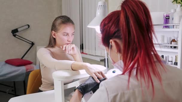 En kvinnlig manikyrist med handskar i skönhetssalong knuffar bort nagelbanden med en träpinne på klientens naglar innan gelen appliceras — Stockvideo