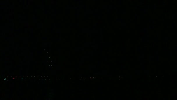 Barevné jiskřičky sváteční ohňostroje na nočním nebi nad řekou, odrážející se ve vodě. Časové skoky. — Stock video