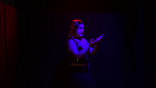 En kvinna i djävulsdräkt med ett illavarslande leende dansar i rött ljus på svart bakgrund. — Stockvideo