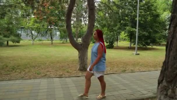 Una mujer camina por una pasarela de piedra en un parque — Vídeos de Stock