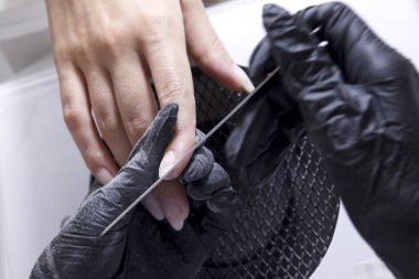 Bir manikürcü müşterinin tırnaklarını cilalar ve kaba jel kaplamaya hazırlanır..