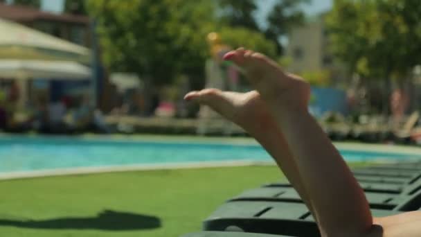 Frauenbeine auf einem Liegestuhl am Pool. — Stockvideo