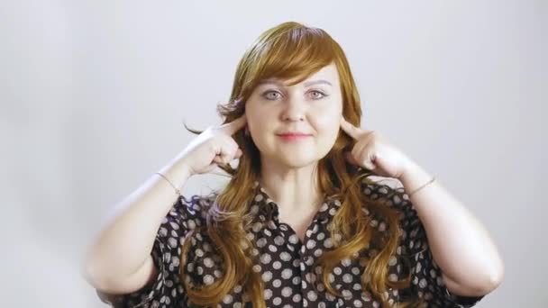 Молодая женщина на белом фоне щекочет уши и показывает свое лицо, что она неприятна в звуке — стоковое видео