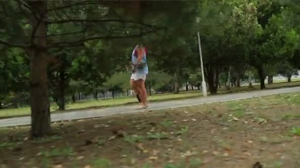 A woman in a park walking along a green alley — Stockvideo