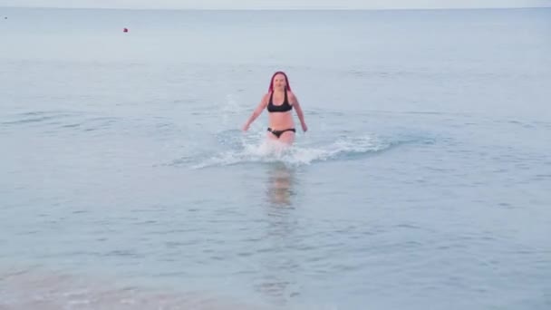 Mujer judía en traje de baño negro con trenzas rojas sale del mar — Vídeo de stock