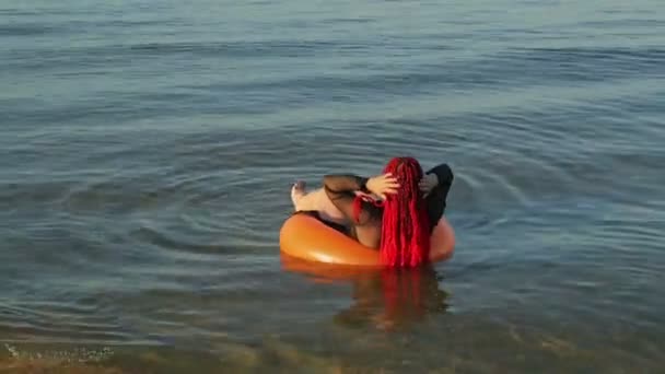 Žena v plavkách na mořských vlnách v plaveckém kruhu plave u břehu. — Stock video