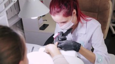 Güzellik salonunda eldivenli bir manikürcü, jel kaplama uygulamadan önce müşteriye manikür yapıyor.