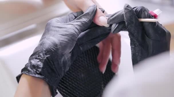 Une femme manucure avec des gants dans un salon de beauté repousse la cuticule avec un bâton de bois sur les ongles du client avant d'appliquer le revêtement de gel — Video