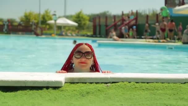 A cheerful woman with red hair on vacation swims to the pool paradise and rests — Stock Video