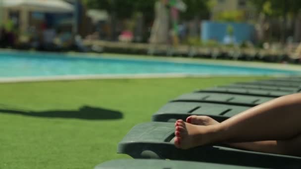 Pernas femininas em uma cadeira de praia junto à piscina . — Vídeo de Stock
