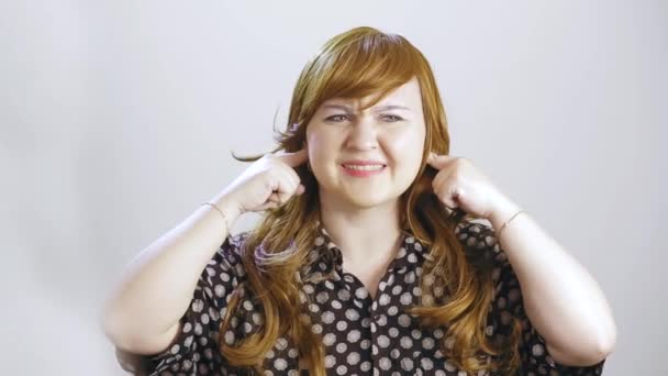 Una joven sobre un fondo blanco se pellizca las orejas y muestra su cara que es desagradable en sonido — Vídeos de Stock