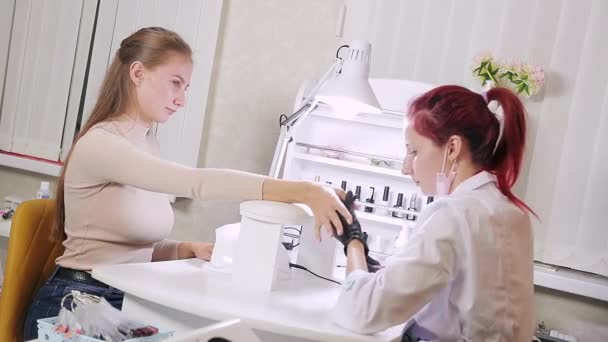 La mujer manicurista en baño cosmético está aplicando gel en las uñas de los clientes. La chica se seca las uñas en una lámpara ultravioleta — Vídeos de Stock