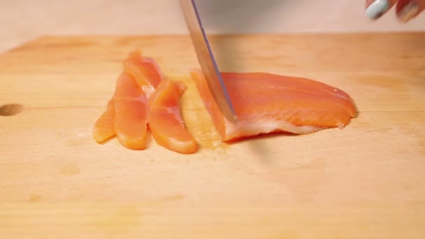 Female hand cuts red trout fish for sandwiches on a wooden board. — Stockvideo