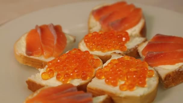 A plate with sandwiches with red fish and red caviar rotates in a circle — Stockvideo