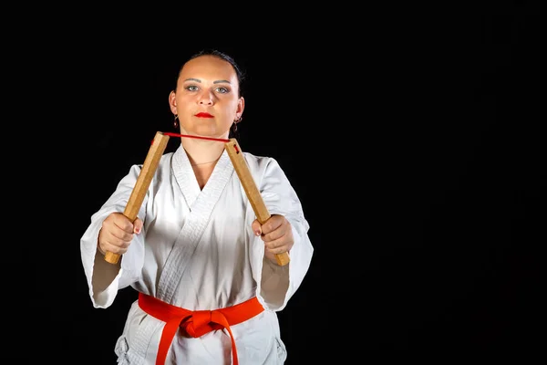 A young brunette woman in a white kimono is engaged with nunchucks on a black background. — Stock Photo, Image
