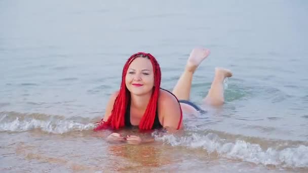 Eine junge Juwelierin mit roten Zöpfen im Urlaub liegt am Meer. — Stockvideo