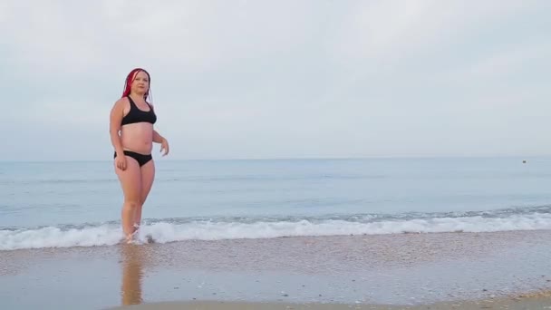 A woman in a black swimsuit comes out of the sea ashore. — Stock Video