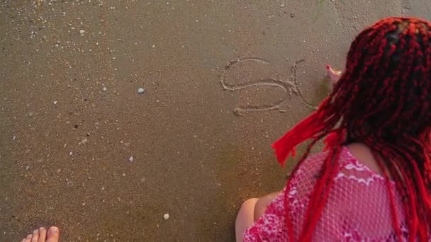 A woman writes in the sand the word co wave is washing away. — Stockvideo