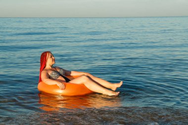 Afrikalı pigtails ile genç bir kadın kıyıya yakın denizde şişme bir daire içinde yüzer.