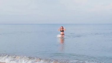 Siyah mayo giymiş bir kadın denizden çıkar.