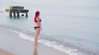 Jewish woman in a black swimsuit with red braids with a run enters the sea