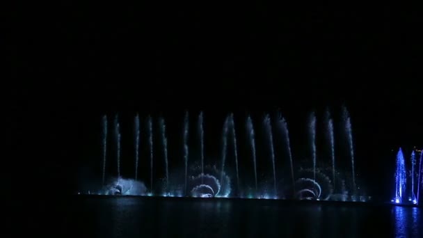 Nachtelijke show van fonteinen schitteren met verschillende kleuren en vormen en reflectie in het water — Stockvideo