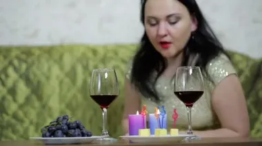 A woman in tears blows out candles and drinks red wine.