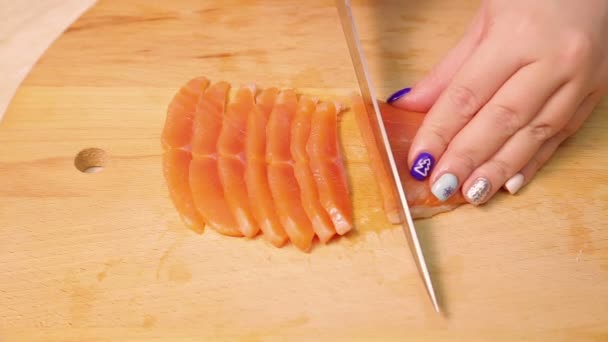 Vrouwelijke hand snijdt rode forel vis voor sandwiches op een houten plank. — Stockvideo