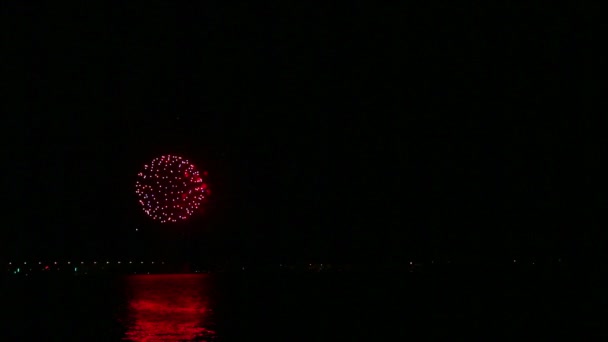 Vuurwerk aan de nachtelijke hemel boven de rivier weerkaatst in het water. — Stockvideo