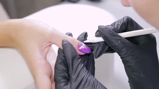 美容院的美容师女人在美容院的指甲上涂上了用莱茵石做的凝胶清漆 — 图库视频影像