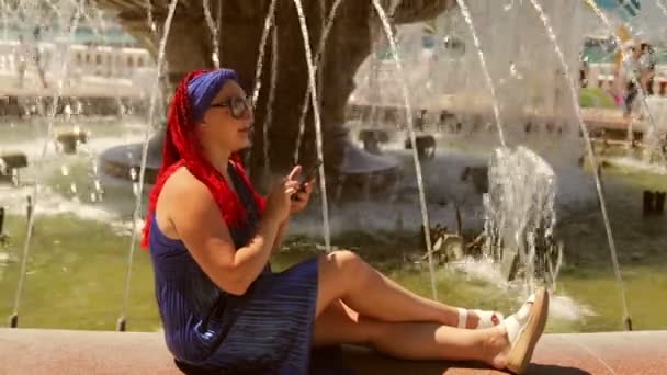 Młoda kobieta na tle fontanny komunikuje się w posłańcu — Wideo stockowe