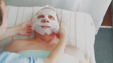 Kadın güzellik müşteri bir spa salonunda yüz maskesi nemlendirici bir adam yapar