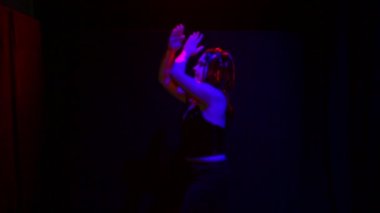 Uğursuz bir gülümsemesi olan şeytan şeklinde bir kadın siyah arka planda kırmızı ışıkta dans eder.