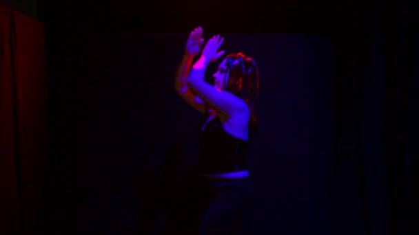 एक महिला एक शैतान के रूप में एक काले पृष्ठभूमि पर लाल प्रकाश में एक अजीब मुस्कान नृत्य के साथ — स्टॉक वीडियो