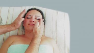 Bir erkek kozmetolojist bir kadın müşteri bir spa salonunda sıkılaşmış yüz masajı verir.