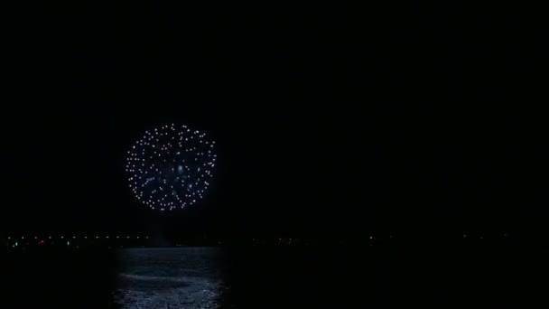Brillantes fuegos artificiales festivos en el cielo nocturno sobre el río con reflejo en el agua . — Vídeos de Stock
