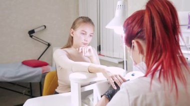 Güzellik salonunda eldivenleri olan bir manikürcü, jel kaplama uygulamadan önce müşterinin tırnaklarına tahta bir sopayla tırnak derisini itiyor.