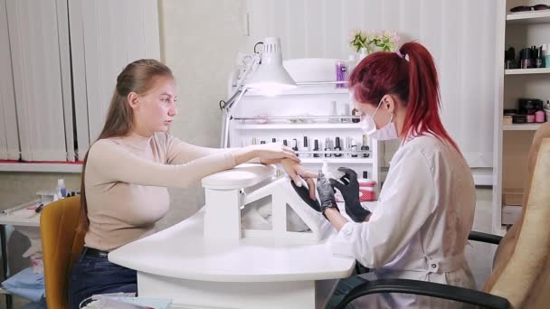 Mujer manicurista con guantes en un salón de belleza pule las uñas de un cliente antes de aplicar gel de recubrimiento — Vídeo de stock