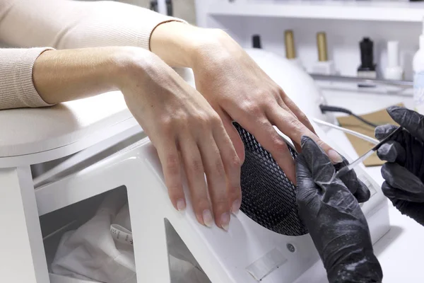 Manikürcü elleri muayene eder ve müşterilerin tırnaklarını cilalar..