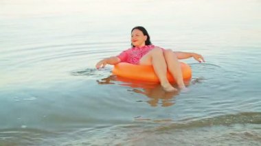 Kumral bir kadın kıyıya yakın bir denizde yüzme çemberinde gülümsüyor..