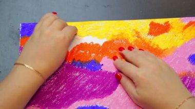 Bir kadın turuncu tebeşirle gün batımında pastel gökyüzü manzarasını tamamlıyor.