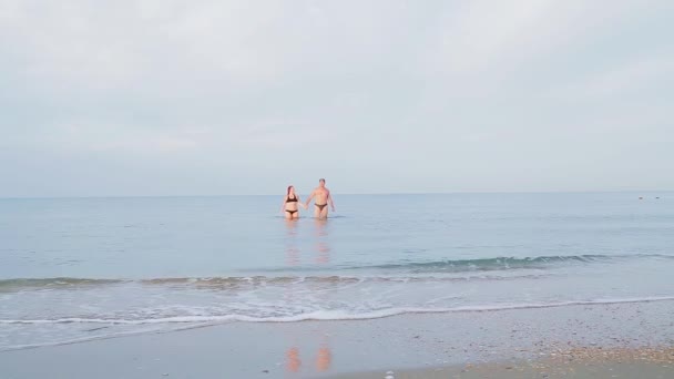 Ein Mann und eine Frau gehen Händchen haltend auf dem Meerwasser — Stockvideo