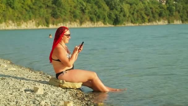 携帯電話で湖を走っている夕日の若い日焼けした女性. — ストック動画